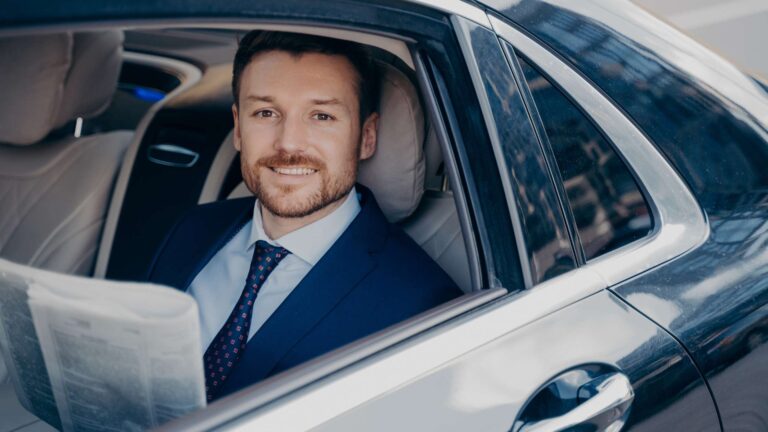 Man in suit smiling in car with newspaper