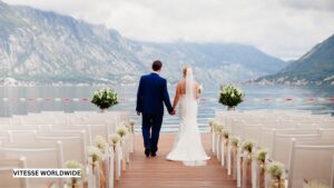 Couple walking down the aisle at a lakeside luxury destination wedding, having arrived there by private jet and chauffeured luxury vehicle, symbolizing elegant, first-class celebration travel.