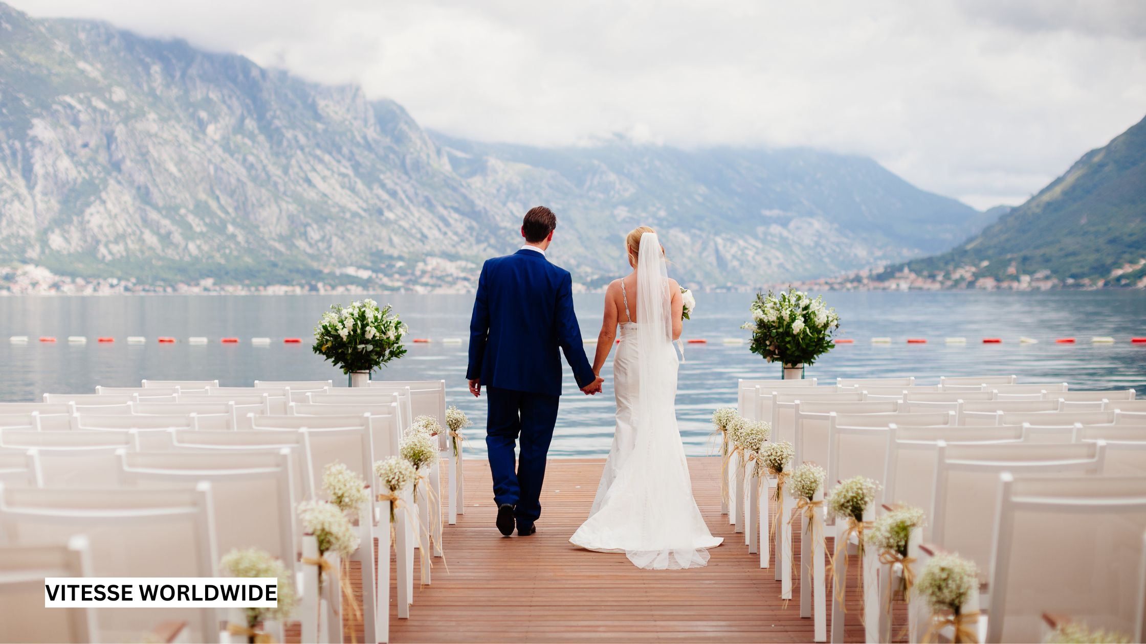 Couple walking down the aisle at a lakeside luxury destination wedding, having arrived there by private jet and chauffeured luxury vehicle, symbolizing elegant, first-class celebration travel.