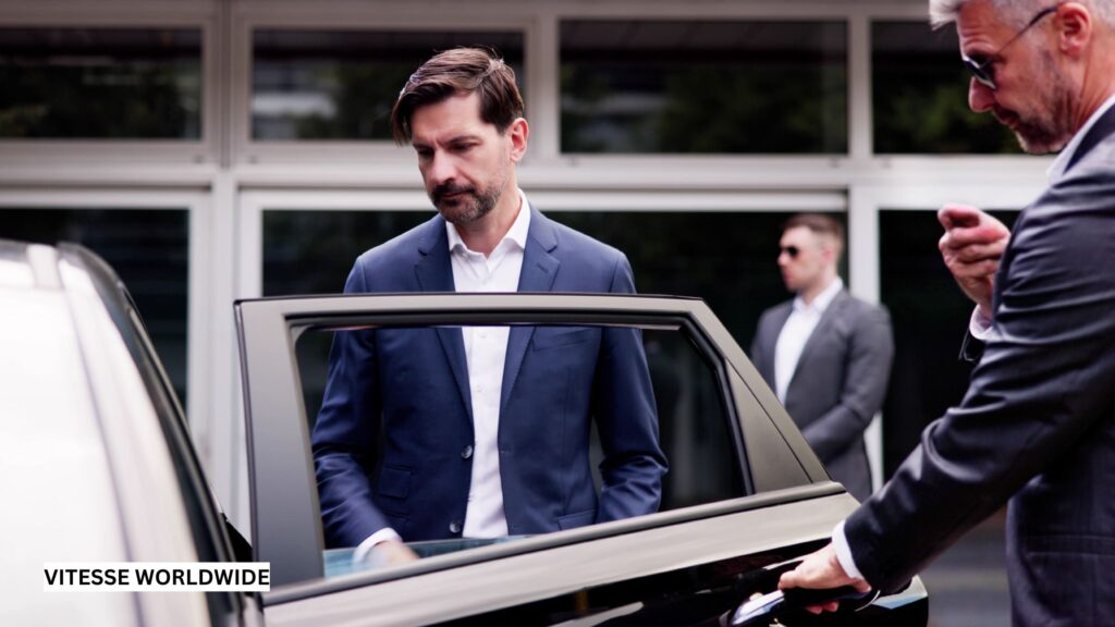 VIP person being ushered into a black luxury sedan by a professional chauffeur in a suit, standing outside a modern arena, conveying exclusivity and premium service.