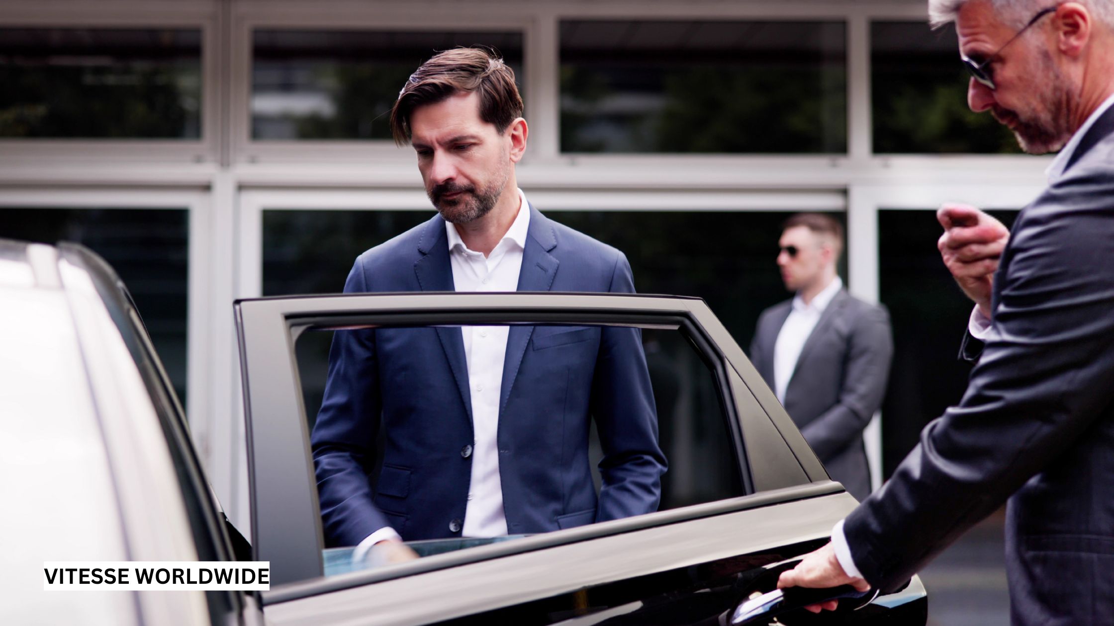 VIP person being ushered into a black luxury sedan by a professional chauffeur in a suit, standing outside a modern arena, conveying exclusivity and premium service.